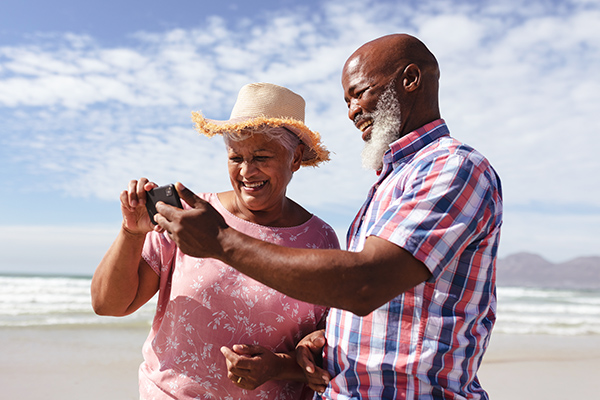 Happy senior couple using smartphone at the beach