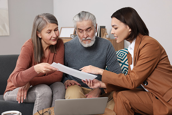 An insurance agent sits next to elderly couple and shows them pension plan documents