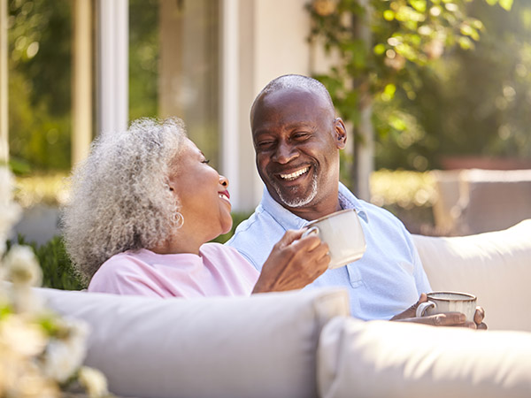 Retired Couple Sitting Outdoors At Home Having Morning Coffee Together